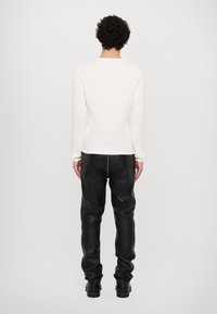 Hvid langærmet top med en struktureret overflade, parret med sorte læderbukser med en central søm og tapered ben.