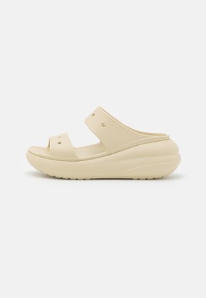 Sandale beige à enfiler avec deux brides et perforations, dotée d'une semelle épaisse et rembourrée avec un talon arrondi et une semelle intérieure texturée.