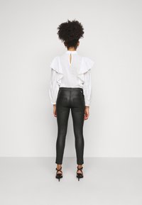 Blusa branca com volantes, com um detalhe em forma de buraco nas costas e tecido texturizado, combinada com calças de couro pretas, justas ao corpo, e sapatos de salto alto com tiras.