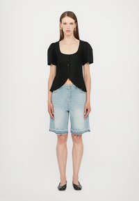 Svart cropped topp med korte pufferm og fire knapper, parret med lyseblå denimshorts med frynsete kanter og en løs passform.