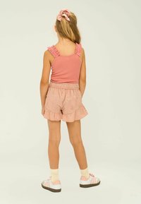Rosa ribbad topp med volangärmar, ihop med rosa blommiga shorts med volanger vid nederkanten. Vita sneakers med rosa detaljer.