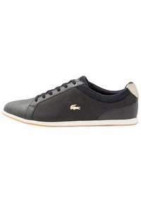 Svart låg sneaker med svarta snören, vit sula, beige hälltab och liten beige krokodil-logotyp på sidan.