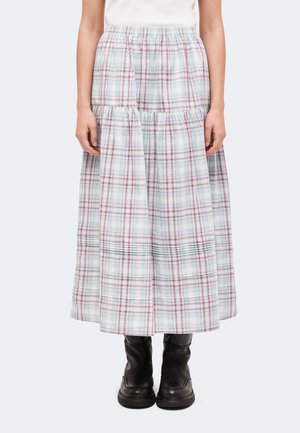Personne portant une jupe midi à carreaux bleu clair et rouge avec des détails froncés et des bottines noires, debout devant un fond uni.