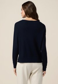 Ciemnoniebieski sweter typu pulower o luźnym kroju, okrągłym dekolcie i długich rękawach; cechuje go gładka tekstura i ściągacze przy mankietach.
