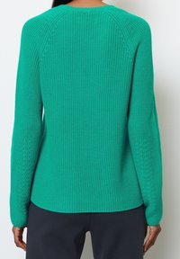 Pull en tricot vert avec une finition texturée, doté d'un col rond et de manches longues, se prolongeant jusqu'à un ourlet légèrement courbé.