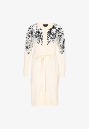 Krémové dlouhé kardigánové šaty s rukávy, zdobené stříbrnými a černými flitry na ramenech a horní části hrudníku, s páskem v oblasti pasu.