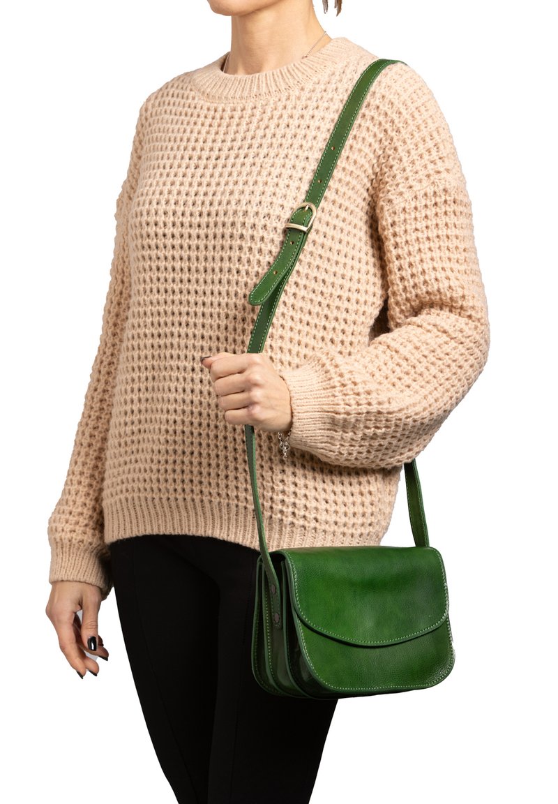 Borsa a tracolla verde in pelle con chiusura a pattina, forma strutturata, tracolla regolabile e texture liscia. Indossata sopra un maglione chiaro.