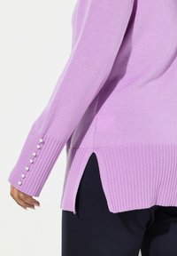 Lila gestrickter Pullover mit gerippten Seitenschlitzen und langen Ärmeln, verziert mit Perlenknöpfen entlang des linken Ärmels und einer weichen Textur.