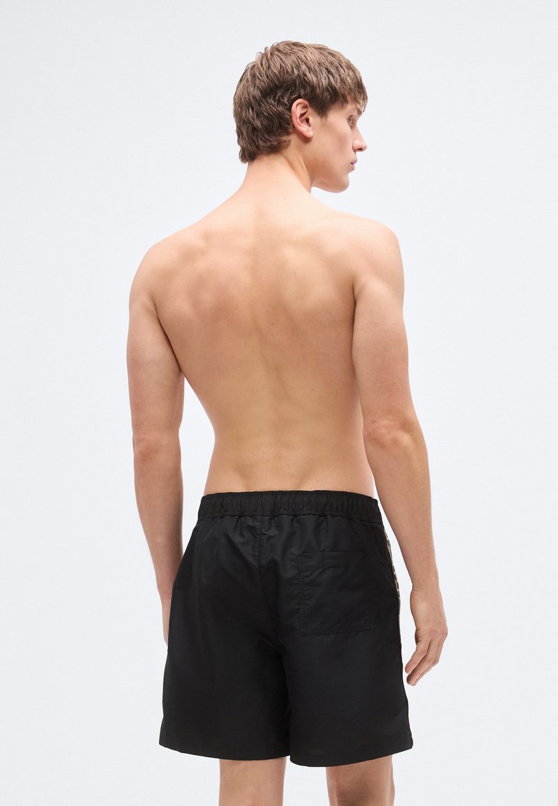 Shorts de bain noirs avec une ceinture élastique, une poche arrière et un tissu lisse et léger. Les shorts ont une coupe classique et décontractée.