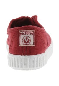 Sneaker di tela rossa con suola in gomma bianca, vista dal retro, con etichetta del marchio "Victoria" sul tallone.