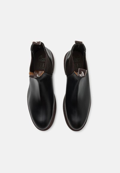 Mustad nahast loaferid elastsete külgpanelidega, mandli kujuline varvas, pruun nahkdetail ning nööpidega kaunistus tallal.