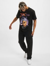 Sort bomulds t-shirt med et stort 2Pac-tryk i lilla accenter. Samlet med sorte bukser og hvide sneakers. Casual pasform og stil.