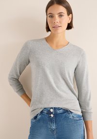 Ljusgrå V-ringad tröja med ribbade manschetter och en slät yta, kombinerad med blå denimjeans med knappdetaljer.