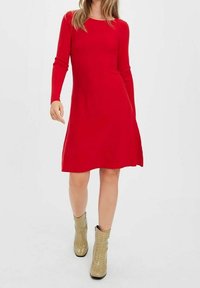 Robe rouge à manches longues avec un haut près du corps et une jupe évasée. Tissu tricoté avec une texture lisse, associée à des bottines dorées métalliques.