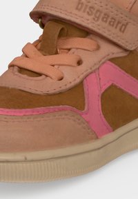 Gros plan d'une basket marron et rose avec des lacets pêche, un détail latéral rose, une semelle beige et une bride étiquetée "bisgaard."