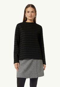Czarna bluzka z długim rękawem w wzór houndstooth z okrągłym dekoltem, w połączeniu z szaro-skalanym spódnicą. Gładka faktura, luźny krój.