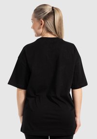 Camiseta negra de gran tamaño con mangas cortas, hecha de algodón, con un cuello redondo y una textura suave. Sin patrones de diseño visibles.