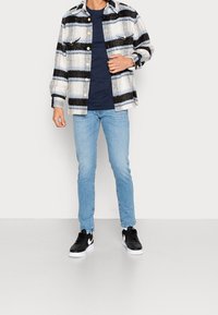 Rutig flanellskjorta i grått, blått och svart, bärs över en marinblå t-shirt, kombinerad med ljusblå jeans och svarta sneakers.