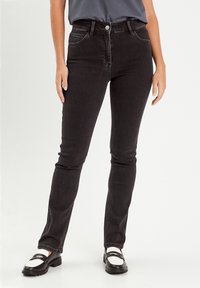 Jean en denim noir à coupe slim, taille mi-haute, design à cinq poches et coutures contrastées. Portés avec des chaussures noires et blanches.