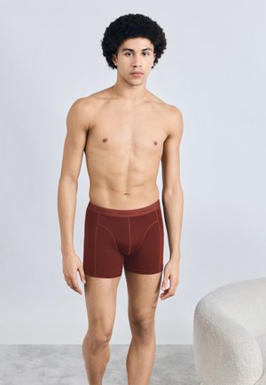 Ανδρικά μπορντό μποξεράκια, κατασκευασμένα από λείο ύφασμα, με εφαρμοστή σχεδίαση και διακριτικές ραφές γύρω από τη μέση και τα πόδια.