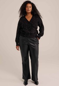 Črna ovita jopica s srebrnimi pikami, dolgi rokavi in rebrastimi manšetami, v kombinaciji s črnimi visokotlačnimi usnjeni hlačami in dolžinskimi petami.