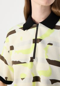 Knit polo shirt with a quarter-zip, featuring a black collar and a pattern of light yellow, brown, and cream stripes. Textured fabric.