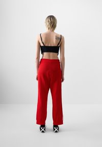 Musta lyhyt toppi säädettävillä olkaimilla, yhdistettynä löysästi istuviin, teksturoituihin kirkkaanpunaisiin housuihin ja mustiin urheilukenkiin, joissa on valkoisia yksityiskohtia.