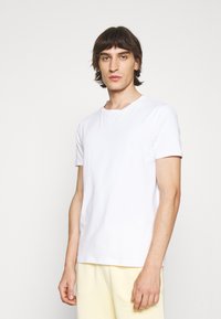 Tricou alb cu mânecă scurtă, fabricat din bumbac moale, cu decolteu rotund, având un design simplu și o croială standard.