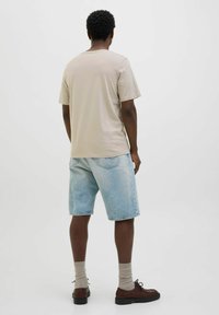 Camiseta de algodón beige, pantalones cortos de mezclilla azul claros, calcetines beige, zapatos marrones y peinado texturizado, visto desde atrás.