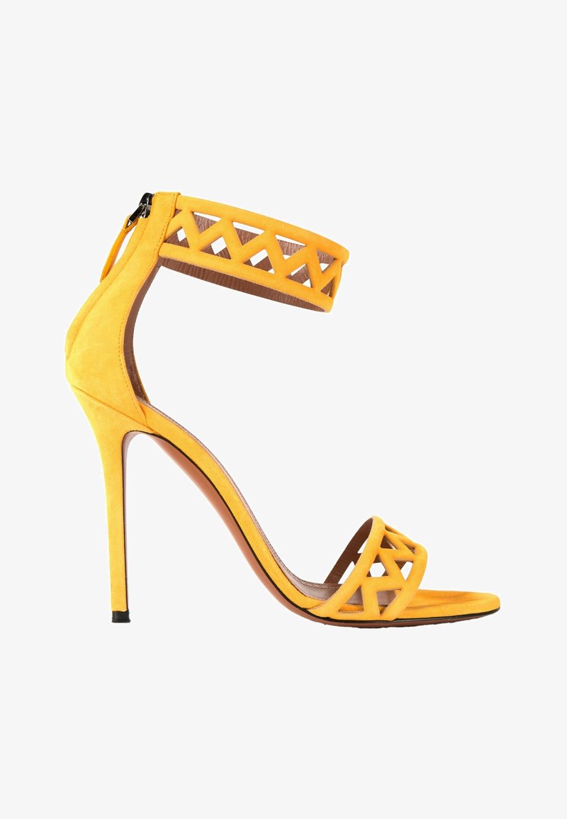 Sandale jaune à talons hauts avec bride à la cheville et bride aux orteils présentant un motif géométrique découpé, et fermeture éclair à l’arrière.