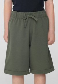 Shorts de sport vert olive avec une surface texturée, taille élastique et lien à l'avant. L'ourlet retroussé ajoute un détail ; pas de poches visibles.