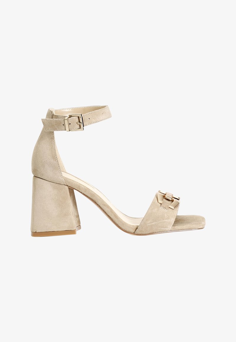 Sandali a tacco in suede beige con tacco a blocco largo, cinturino alla caviglia e decorazioni in oro sulla parte anteriore del cinturino. Texture liscia e design minimalista.