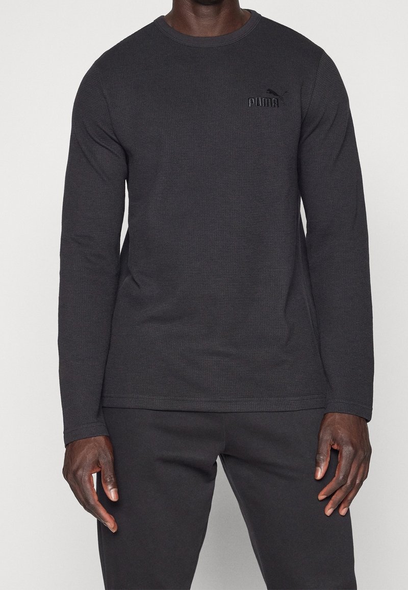Schwarzes langärmliges Baumwoll-T-Shirt mit strukturiertem Muster, Rundhalsausschnitt und gesticktem Puma-Logo auf der Brust. Kombiniert mit schwarzen Hosen.