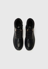 Bottines hautes en cuir noir avec un col nervuré, bout rond et œillets en laiton. Présente des lacets noirs et un détail de fermeture éclair sur le côté.