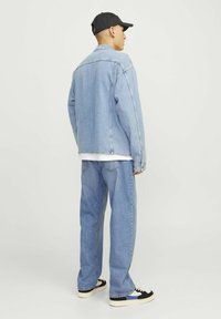 Lichtblauwe denimjack en bijpassende broek, relaxed fit, met een wit shirt eronder, gecombineerd met zwart-witte sneakers en een zwarte pet.