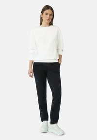 Witte sweatshirt met ronde hals en lange mouwen, gecombineerd met zwarte tapered broeken. Model draagt witte chunky sneakers. Minimalistisch ontwerp.