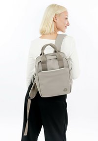Šedý batoh s dvojitými horními uchy a nastavitelným popruhem, který se vyznačuje elegantním designem, přední kapsou na zip a logem na boku.