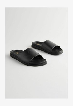 Crne natikače imaju teksturiranu gornju traku od umjetne kože i glatki đon, dizajnirane za jednostavno obuvanje i udobnost.