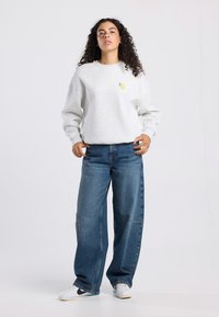 Light gray sweatshirt with a small yellow lemon graphic on the chest, paired with loose blue denim jeans and white sneakers.