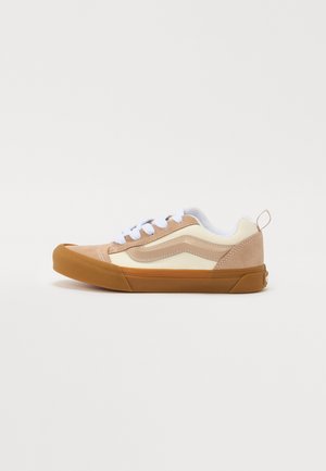 Barna és krémszínű sneaker velúr és bőr felsőrésszel, fehér cipőfűzőkkel, gumitalppal, valamint kontrasztos barna lábujj- és sarokdísszel.