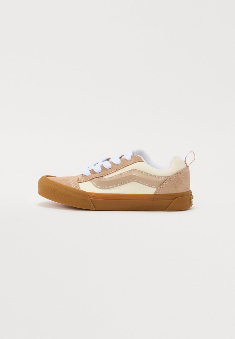 Sneaker beige et crème avec une tige en daim et cuir, lacets blancs, semelle en caoutchouc et un capuchon de orteil et un accent au talon marron contrastants.