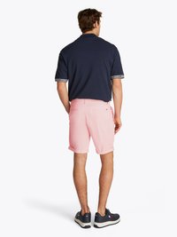 Polo de manga curta azul-marinho, calções rosa com punhos dobrados e ténis escuros com solas brancas; marcação mínima nas mangas da camisa.