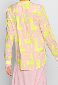 Camisa de manga larga en amarillo brillante y rosa, con un patrón impreso audaz, dobladillo curvado y puños a rayas. Fabricada en algodón.