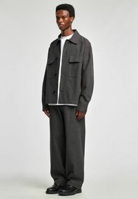 Szara, oversize marynarka w cienkie prążki z naszywanymi kieszeniami, noszona na białej koszulce, zestawiona z dopasowanymi szerokimi spodniami i czarnymi butami.