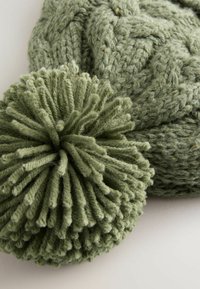 Berretto verde a maglia con un grande pom-pom in cima, caratterizzato da un motivo texture e filato morbido e spesso.