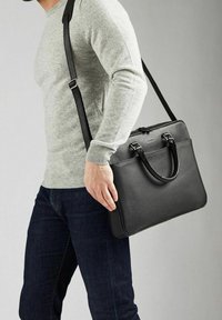 Sort læderportefølje med to håndtag og en justerbar skulderrem. Struktureret overflade med et elegant, rektangulært design.