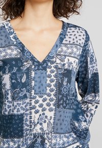 Haut à manches longues avec un col en V, réalisé dans un tissu à motifs dans des nuances de bleu et blanc, avec des dessins cachemire et floraux.