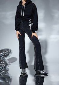 Černá mikina s bílými šňůrkami a šněrovacími detaily po stranách, spojená s rozšířenými černými kalhotami s jemným třpytivým efektem a stříbrnými podpatky.