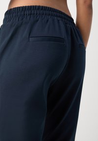 Donkermarineblauwe joggers met een gladde stof, elastische tailleband en twee achterzakken. Eenvoudig ontwerp met een losse pasvorm voor comfort.