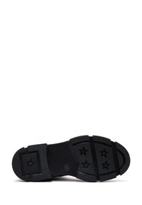 Suola di scarpa in gomma nera con grip testurizzato, decorata con motivi a stella. Presenta sezioni segmentate per flessibilità e trazione.